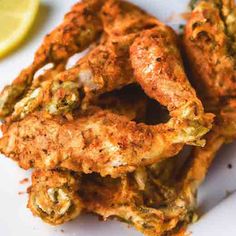 some fried food on a white plate with lemon wedges