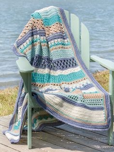 a crocheted blanket sitting on top of a green chair next to the ocean