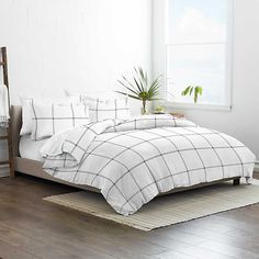 a bed with white and black plaid comforter in a room next to a window