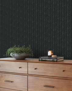 a wooden dresser topped with books next to a wallpapered black and white pattern