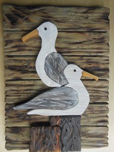 two seagulls sitting on top of a wooden post with wood planks in the background