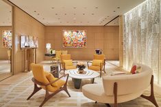 a living room filled with yellow chairs next to a wall covered in glass panels and artwork