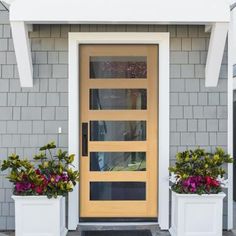 two white planters with flowers in front of a yellow and black door on a gray brick house