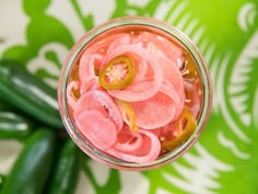 a jar filled with pickles on top of a green and white table cloth next to cucumbers