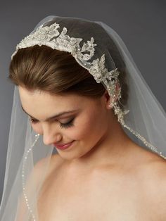 a woman wearing a veil with flowers on the side and pearls in the middle is looking down at her face