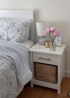 a white bed with blue and pink flowers on the night stand, next to a nightstand