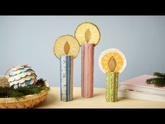 three decorative candles sitting on top of a table next to an easter basket and books