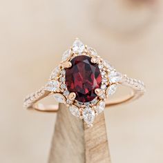 a ring with a large red stone surrounded by white and yellow diamonds on a wooden stand