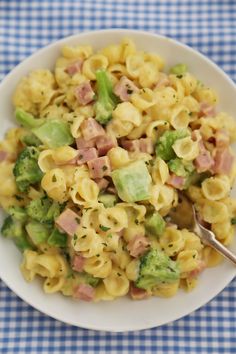 a white bowl filled with macaroni and broccoli on top of a blue checkered table cloth