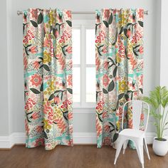 a white chair sitting in front of a window covered in colorful floral curtain panels and valances