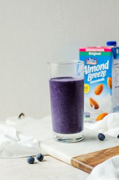 a glass filled with blueberries next to a carton of almonds and milk