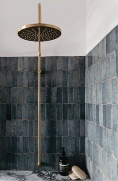 a shower head in a bathroom with blue tiles on the walls and floor, along with a gold faucet