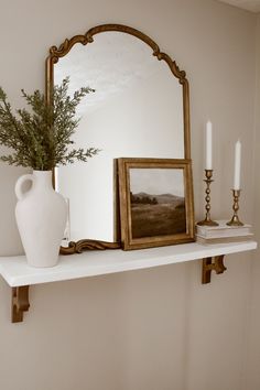 a white vase sitting on top of a shelf next to a mirror and candle holder