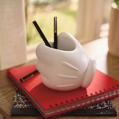 a white vase sitting on top of a red book next to a pen and pencil holder