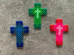 three different colored plastic beads are placed on the ground, one is shaped like a cross