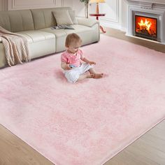 a baby sitting on the floor in front of a fireplace with pink carpet and rug