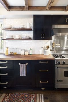 a kitchen with black cabinets and white subway backsplash, stainless steel stove top