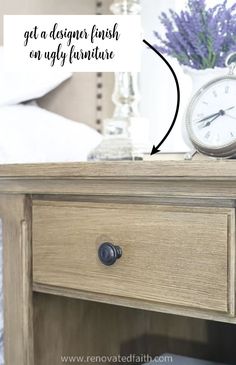 a clock sitting on top of a wooden table next to a bed with white sheets