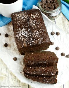 two slices of chocolate banana bread on a plate next to a cup of coffee and bananas