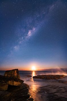 the night sky with stars above water and rocks