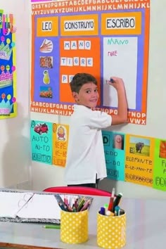 a young boy writing on a whiteboard in front of colorful bulletin boards and pencils