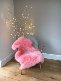 a pink chair sitting in front of a tree with lights on the wall behind it