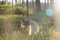 a woman standing in tall grass near trees