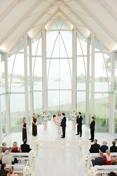 a couple getting married at their wedding ceremony in front of large windows with white flowers and greenery