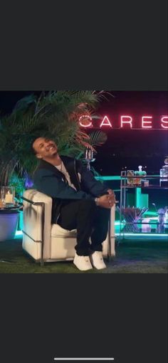 a man sitting on top of a white chair in front of a neon sign