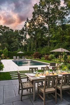 an outdoor dining table with chairs and umbrellas next to a swimming pool at sunset