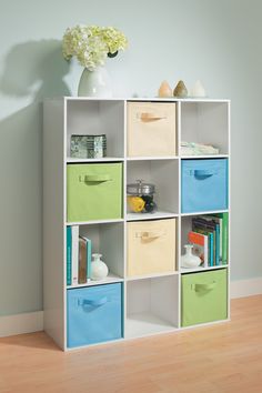 a white bookcase with multicolored bins in front of a flower vase