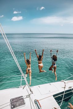 three women jumping off the back of a boat into the ocean with their arms in the air