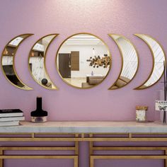 three circular mirrors mounted to the wall above a table with books and vases on it