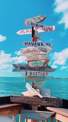 a wooden sign post with many different signs on it's sides and the ocean in the background