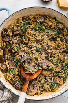 a skillet filled with pasta and mushrooms on top of a white table next to sliced cheese