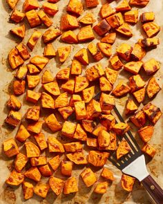 a wooden cutting board topped with cut up sweet potatoes and a spatula next to it