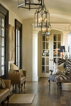 a living room filled with furniture and a chandelier hanging from the ceiling over a wooden floor