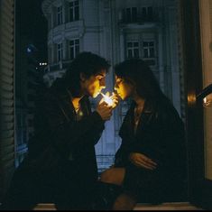 two people sitting on a window sill looking at their cell phones in the dark