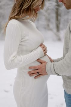 a pregnant woman standing next to a man in the snow with her hands on her stomach