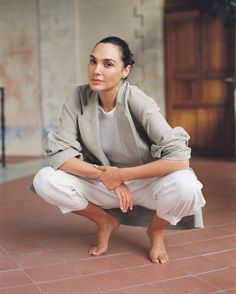 a woman sitting on the ground in white pants and a gray jacket with her arms crossed