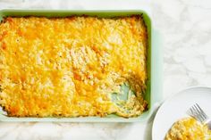 a green casserole dish filled with cheese next to a white plate and fork