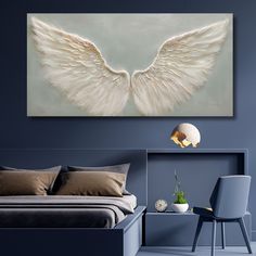 two white angel wings on a wall above a bed in a room with blue walls