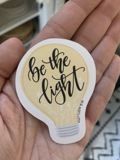 a hand holding a sticker that says be the light