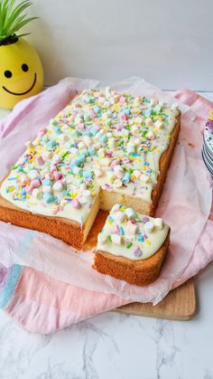 a cake with white frosting and sprinkles sitting on top of a wooden cutting board