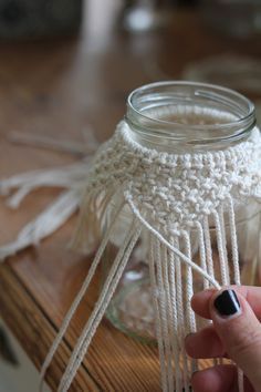 a mason jar with some white yarn hanging from it's side and a hand holding the string