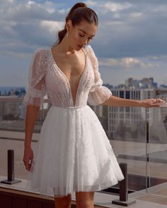 a woman in a short white dress looking down at her hand while standing on a balcony