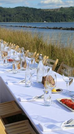 a long table is set with wine glasses, plates and utensils in front of the water