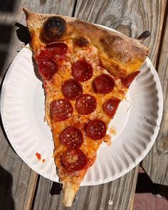 a slice of pepperoni pizza is on a paper plate with a wooden table in the background