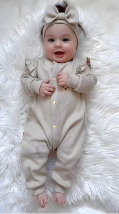 a baby laying on top of a fluffy white blanket wearing a brown outfit with a bow