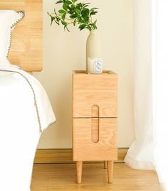 a wooden night stand with a plant on it next to a white bed in a bedroom